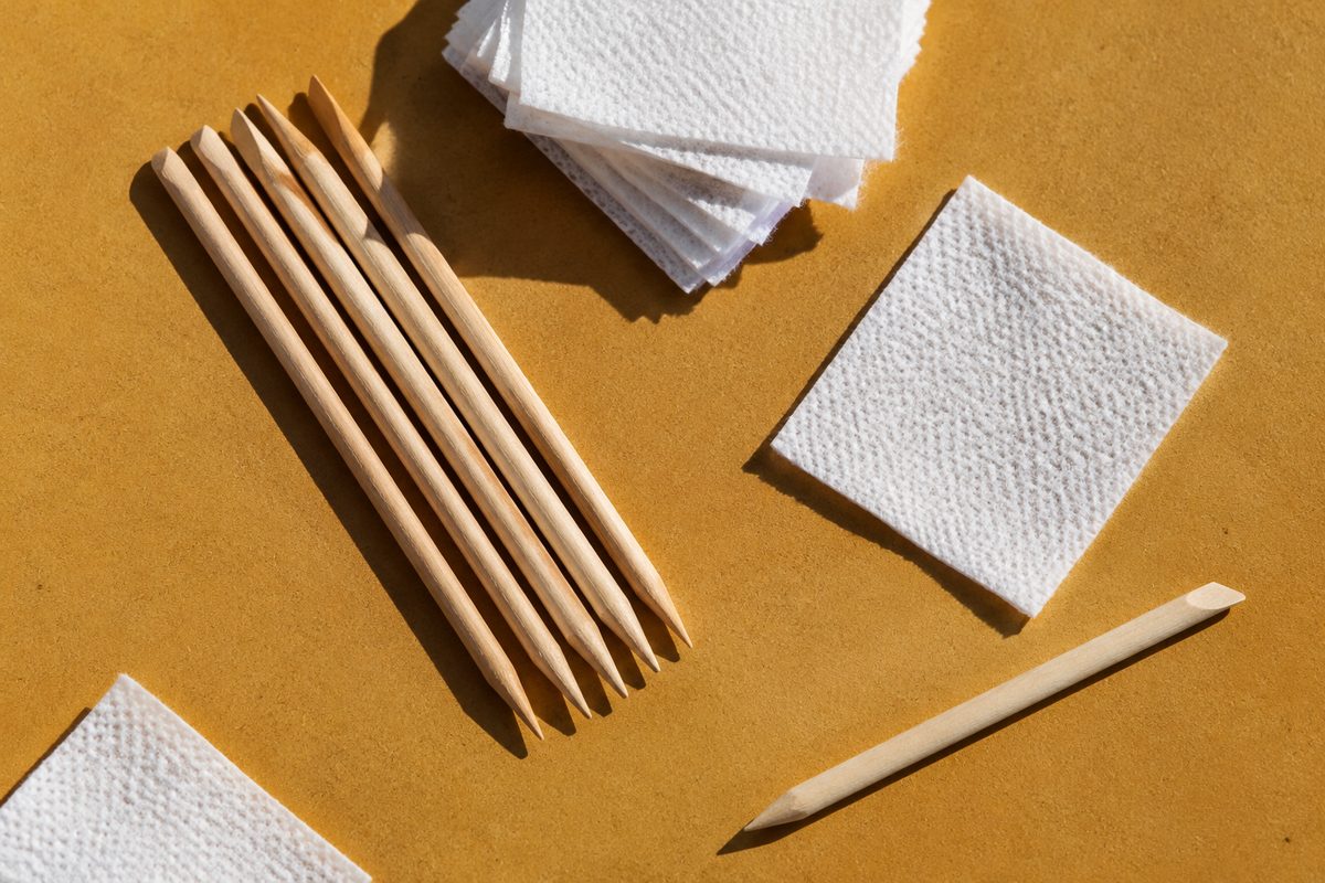 Array of orange wood manicure sticks and sterile wipes on a studio surface