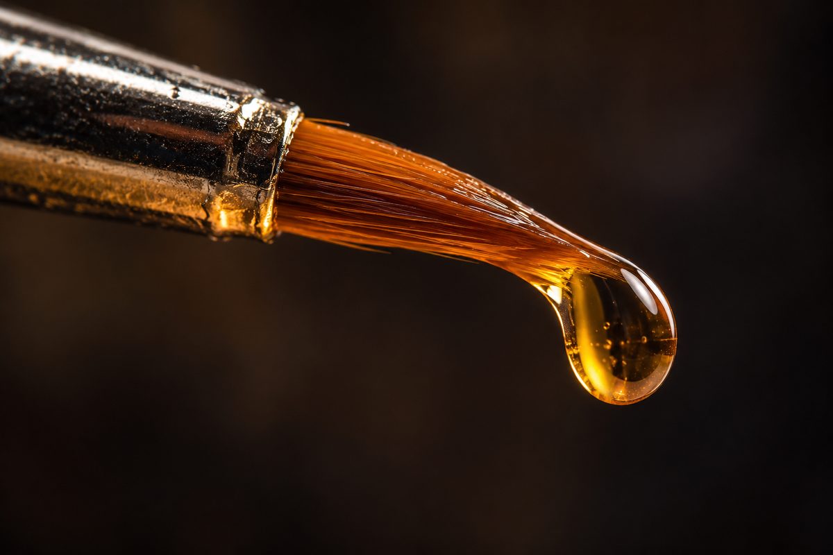 Extreme close-up of a fine nail detail brush with a droplet of clear base coat